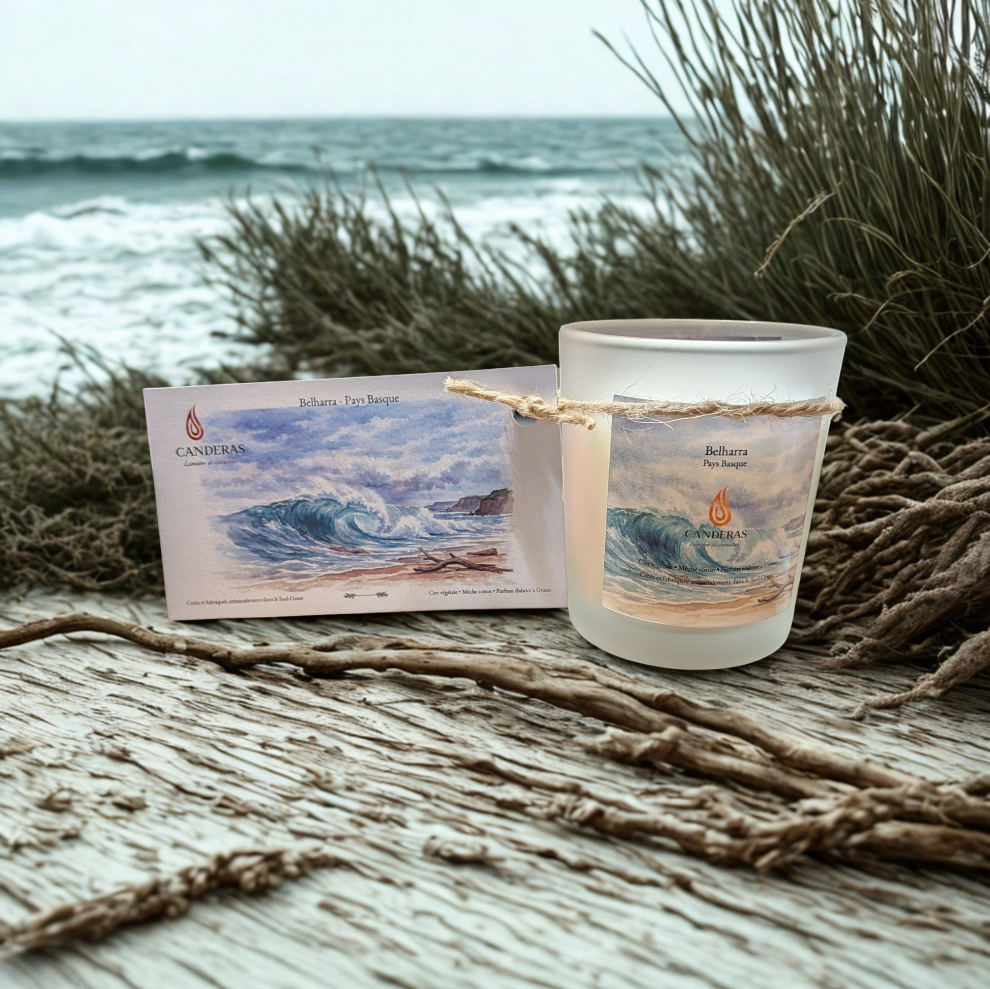 Bougie artisanale du Sud-Ouest Candèras Belharra avec carte postale assortie sur fond bois clair et mur texturé.