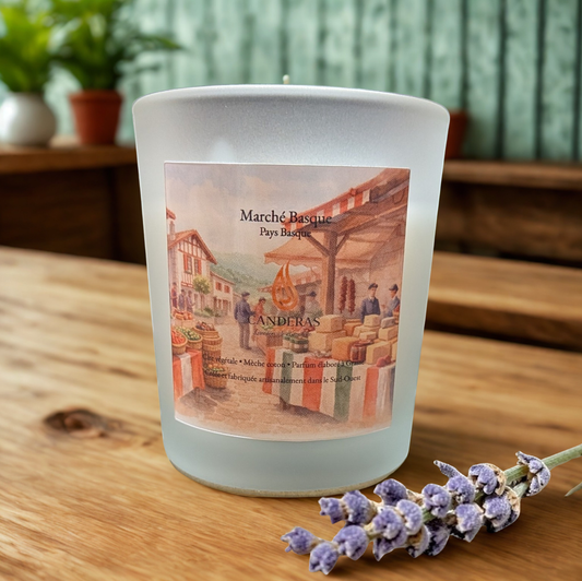 Bougie artisanale du Sud-Ouest Candèras Marché basque en verre givré sur fond bois clair et mur texturé.