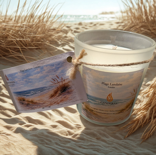 Bougie artisanale du Sud-Ouest Candèras Plage landaise avec carte postale assortie sur fond bois clair et mur texturé.